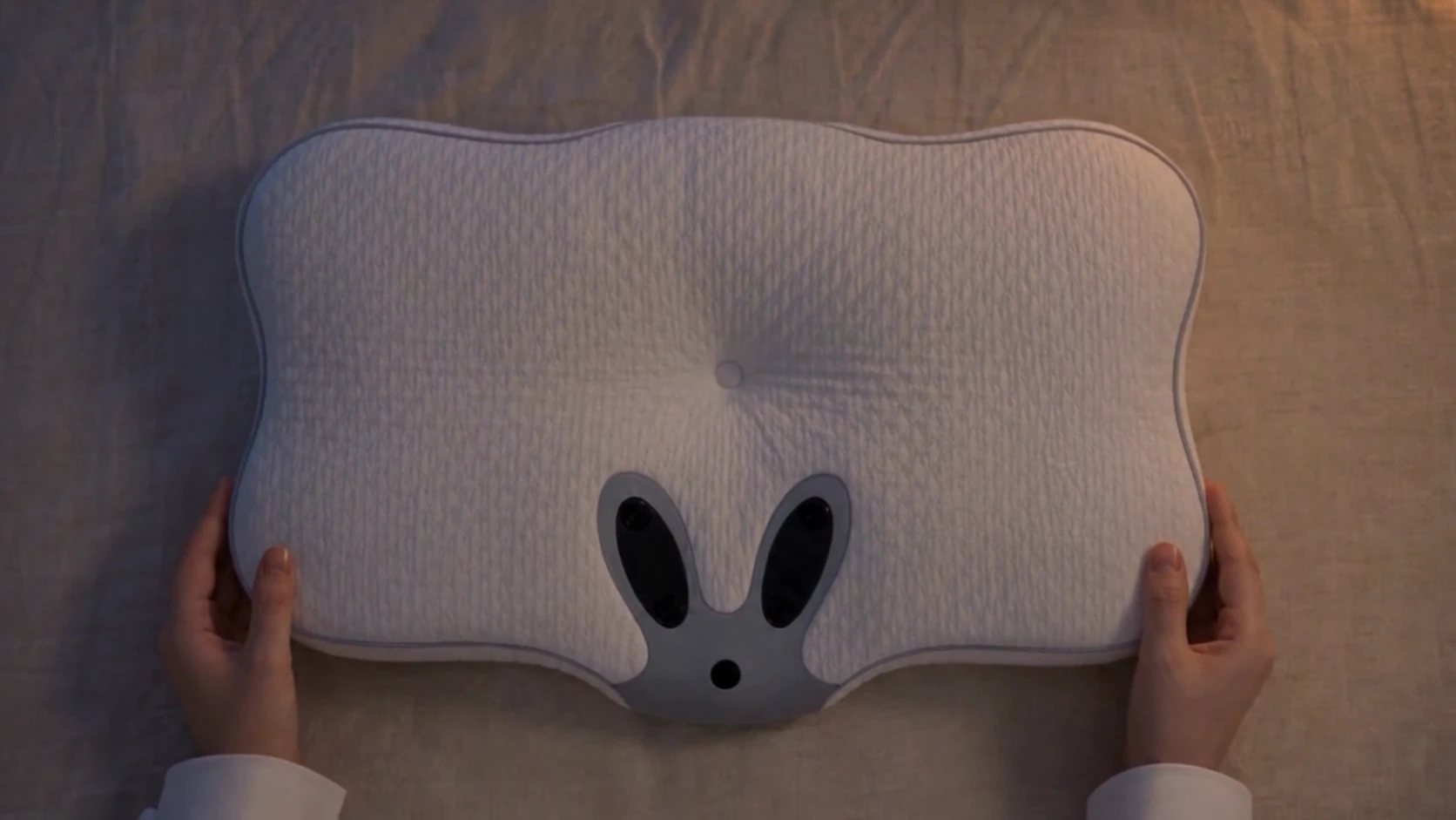 Hands placing the pillow flat on the bed, ready for rest